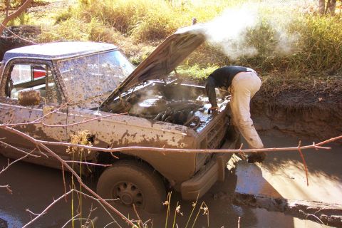 1979 Ford Bronco - A person inspects the engine of a mud-splattered pickup truck stuck in a muddy ditch.