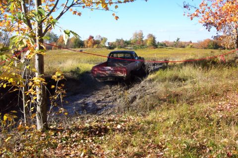 1979 Ford Bronco - A red pickup truck navigates a muddy obstacle course during an off-road event.