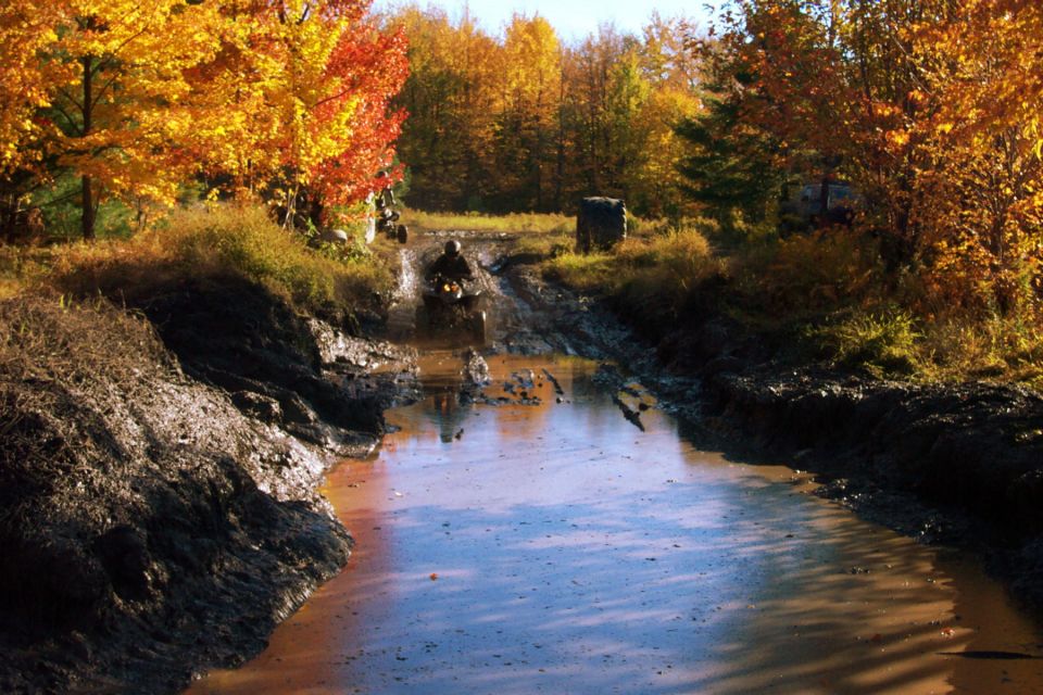 ATV splashing through muddy water with fall foliage in the background