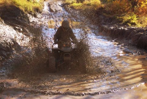 1979 Ford Bronco - An ATV navigates a challenging muddy path, creating a significant splash.