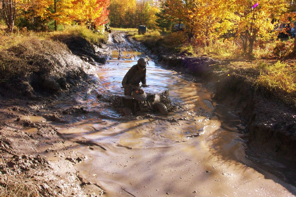 ATV splashing through a muddy ditch with autumn trees in the background