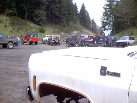 1976 Ford F-100 - Multiple off-road vehicles are parked in a lot near a wooded area.