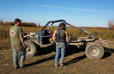 1979 Ford Bronco - A heavily modified off-road vehicle sits in a field with two people nearby under a clear blue sky.