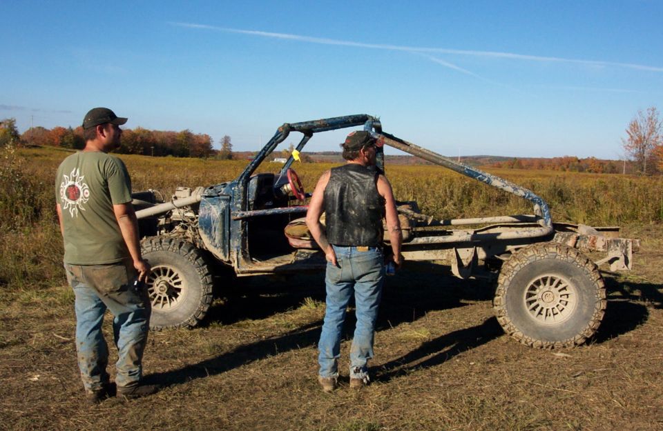 Two guys stand next to a custom buggy with a roll cage and no body panels