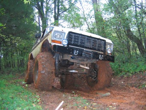 1992 Ford Mustang - A white off-road vehicle is stuck in the mud on a trail surrounded by trees.