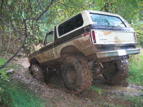 1992 Ford Mustang - This heavily muddied 1978 Ford Bronco is stuck off-road, its large tires digging into the wet ground.