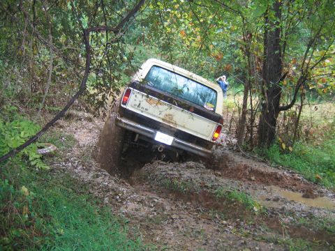 1992 Ford Mustang - A Ford F-Series truck struggles through a muddy off-road course, kicking up dirt and water.
