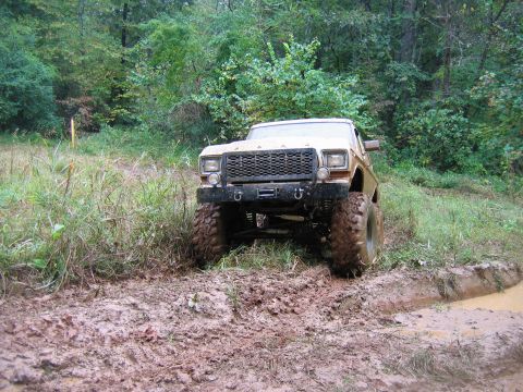 1992 Ford Mustang - Modified pickup truck navigates a muddy off-road trail surrounded by trees.