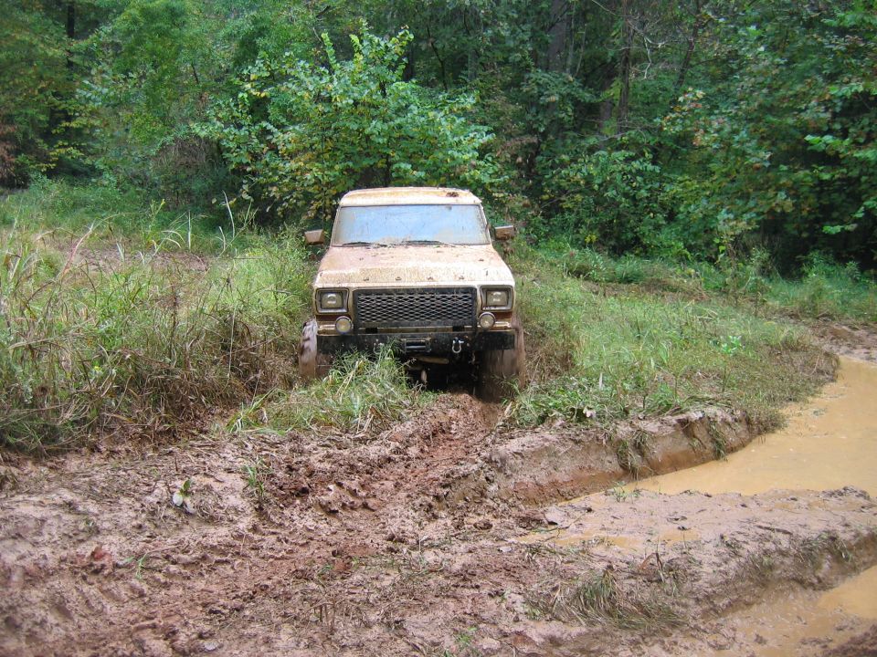 tan off-road vehicle stuck in mud on a trail, trees and brush in background