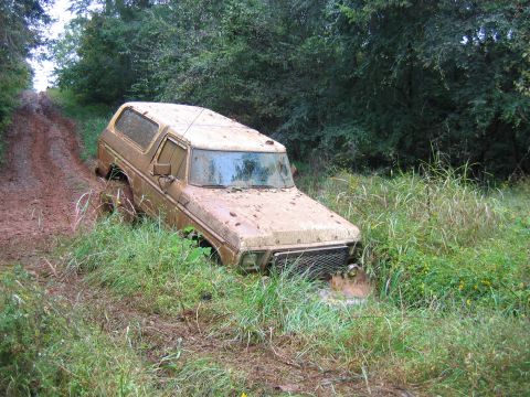 1992 Ford Mustang - A heavily soiled 1978 Ford Bronco is stuck off-road in a muddy area with dense foliage.