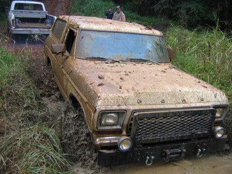1992 Ford Mustang - A heavily mud-covered 1978 Ford Bronco is stuck in a muddy rut on a trail, with another truck visible behind it.