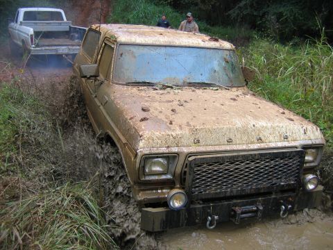 1992 Ford Mustang - Two trucks navigate a muddy trail, one deeply stuck in the mire.