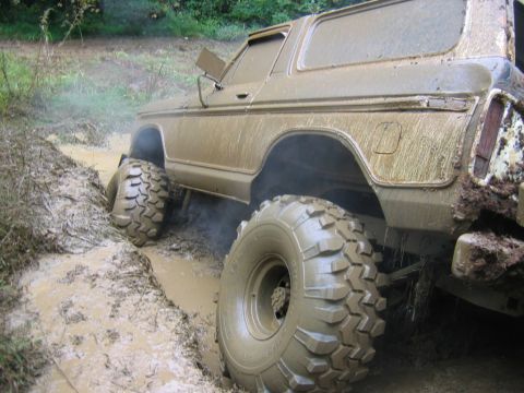 1992 Ford Mustang - This off-road vehicle is deep in mud, with its tires submerged and mud splattered all over its body.