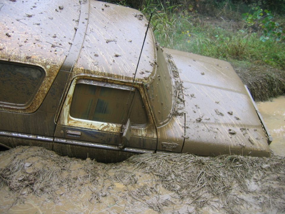 Mud-covered 1978 Ford Bronco stuck in a muddy ditch with vegetation around it