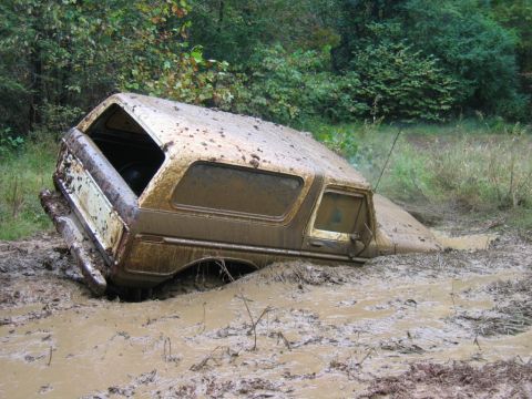1992 Ford Mustang - An off-road vehicle is deeply submerged in thick mud, with only the top and side visible.