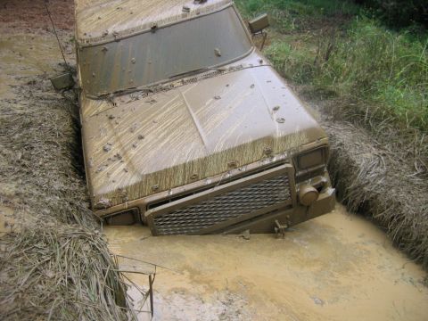 1992 Ford Mustang - A muddy vehicle is stuck in a ditch, with only its front visible above the mud and water.