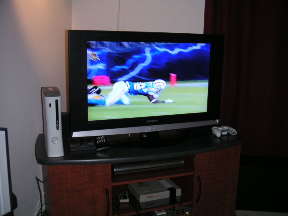 TV displaying a football player on the field, with an Xbox 360 and game consoles nearby