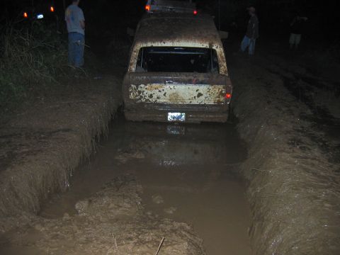 1992 Ford Mustang - A white van is stuck in a deep mud pit on a dirt track at night, with other vehicles and people visible in the background.