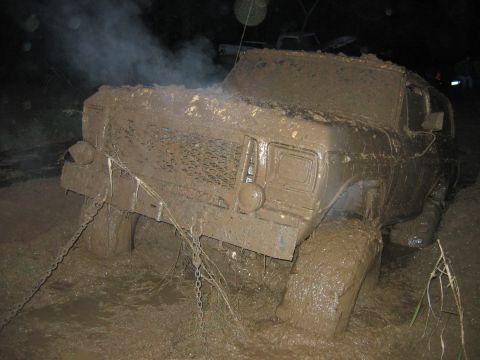 1992 Ford Mustang - An off-road vehicle is deeply stuck in mud, with smoke rising from its engine compartment.