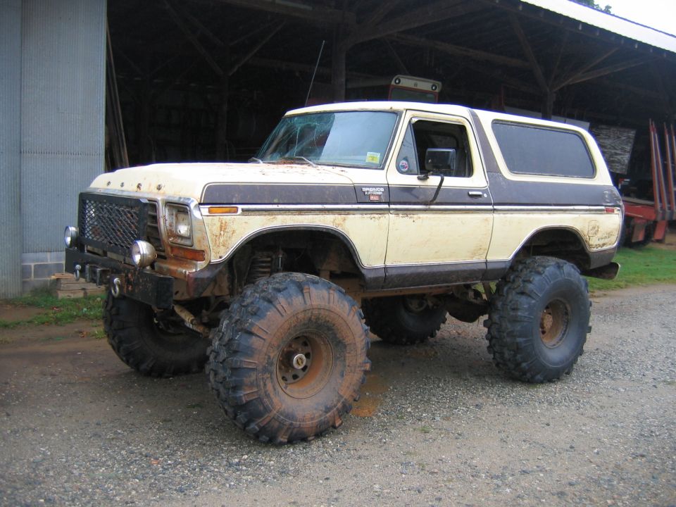 Lifted 1978 Ford Bronco with oversized mud tires, parked in front of a barn
