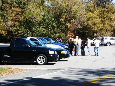 2001 Mercury Grand Marquis - Several vehicles and people gathered in a parking lot on a sunny day with fall foliage.