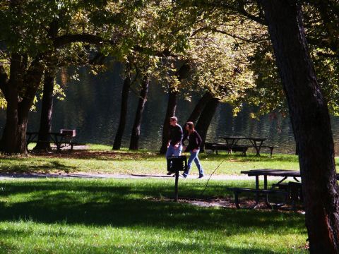 2001 Mercury Grand Marquis - Two people stroll through a park on a sunny day, with picnic tables and a lake in the background.