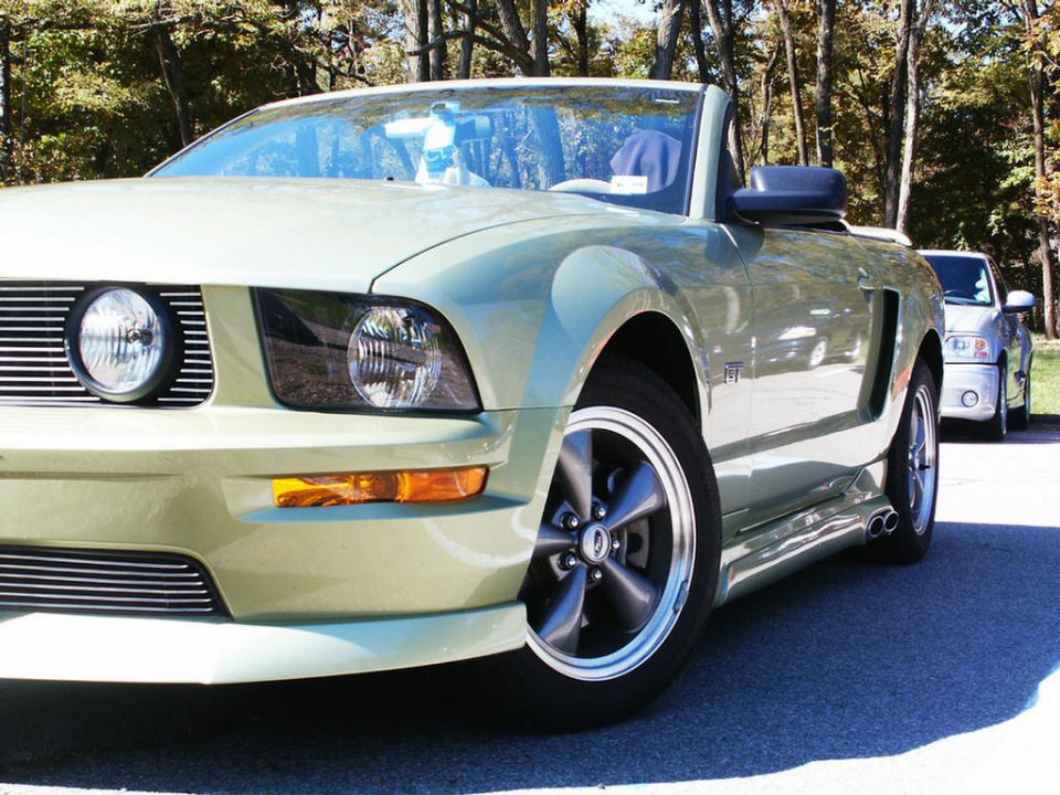 Light green convertible with a black soft top, front passenger side view. A silver SUV is parked behind it