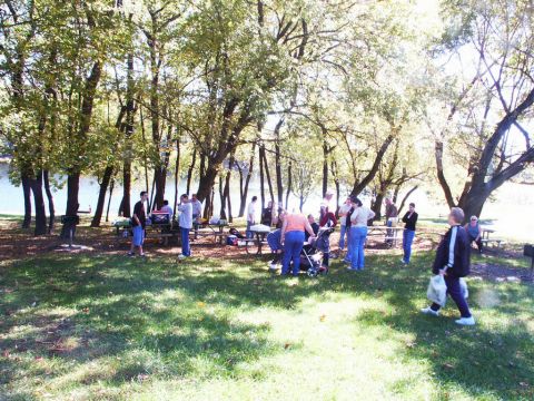 2001 Mercury Grand Marquis - A group of people are enjoying a picnic in a park setting with trees and water visible.