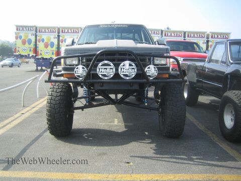 1990 Ford Bronco - Head-on view of a lifted prerunner truck showing its tubular front bumper, four round Hella lights, long-travel suspension and mud tires in…