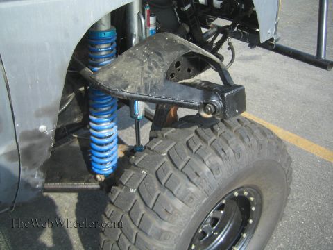 1990 Ford Bronco - close-up of a vehicle's front long-travel suspension featuring a blue coilover spring, bypass shock and a beadlock-rim mud tire.
