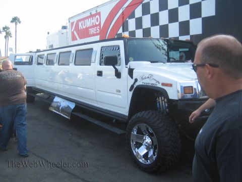1990 Ford Bronco - white stretched Hummer H2 limousine raised on big chrome wheels sits at an outdoor event near a Kumho Tires trailer as men look on.