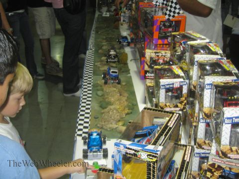 1990 Ford Bronco - Boxed Axle Twister radio-control monster trucks line a vendor table next to an indoor rock-crawling course as a young boy watches an RC tru…