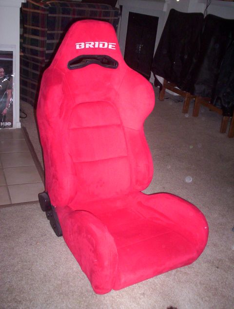 1998 Ford Crown Victoria - red suede Bride reclining bucket racing seat stands on carpet in a room with chairs and a poster in the background.