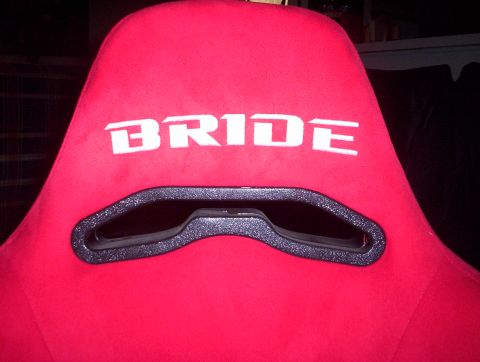 1998 Ford Crown Victoria - Close-up of a red suede Bride racing seat back showing the white BRIDE logo above the harness pass-through opening.