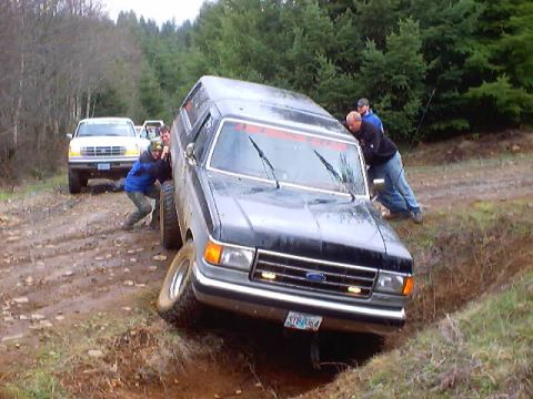 1976 Ford F-100 - People push a stuck Ford truck out of a muddy ditch on a wooded trail.
