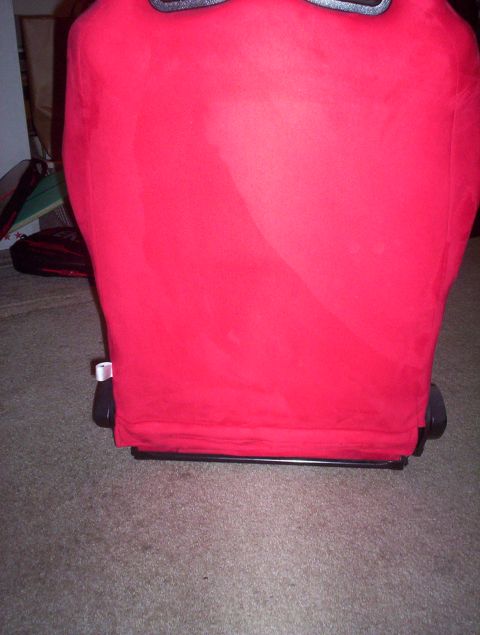 1998 Ford Crown Victoria - Lower rear view of a red suede racing seat showing the seat back and mounting base resting on carpet indoors.