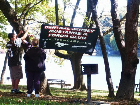 2001 Mercury Grand Marquis - A banner for a car club is displayed outdoors near a lake, with two people adjusting it.