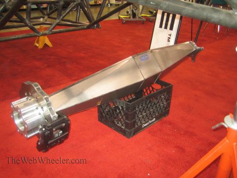 1990 Ford Bronco - long polished aluminum off-road suspension or torque-tube component with a billet end housing rests on a milk crate on red carpet at an ind…