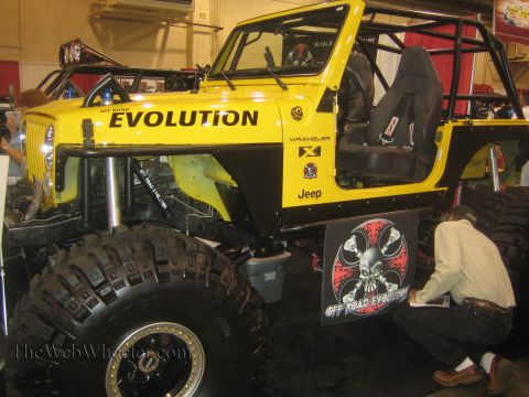 1990 Ford Bronco - bright yellow Jeep Wrangler buggy lettered EVOLUTION, fitted with a roll cage, racing seats and oversized mud tires, sits in an indoor disp…