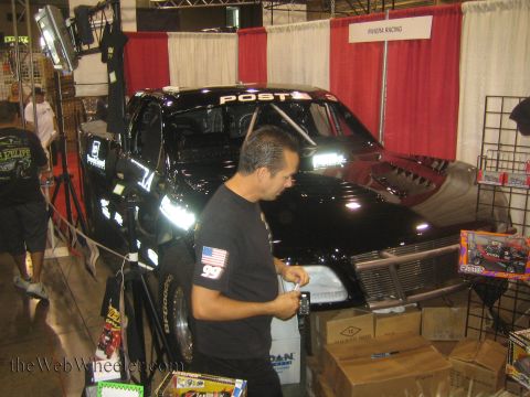 1990 Ford Bronco - black race truck lettered POST sits in a red-and-white curtained booth as a man in a black tee passes by amid product boxes at an expo.