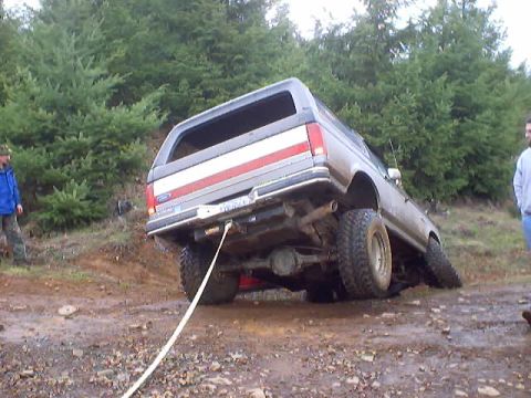 1976 Ford F-100 - A Ford Bronco is stuck on a muddy incline, with a tow rope attached to its rear.