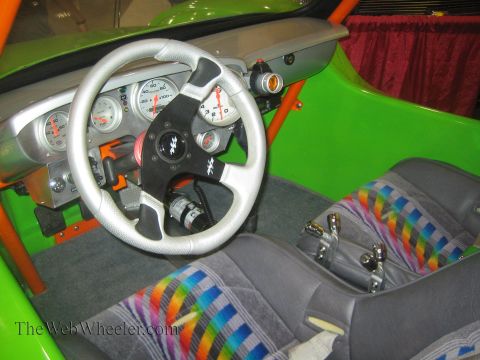 1990 Ford Bronco - green-painted cockpit of a buggy shows a silver steering wheel, round gauges, an orange roll bar and rainbow-striped cloth seats.