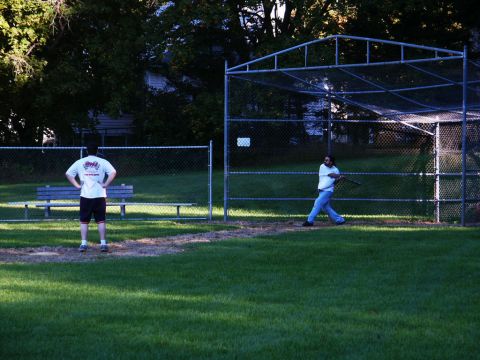 2001 Mercury Grand Marquis - Two men playing baseball in a park with a batting cage and bleachers.