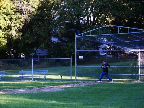 2001 Mercury Grand Marquis - A person practices batting at a baseball field with a chain-link fence and trees in the background.