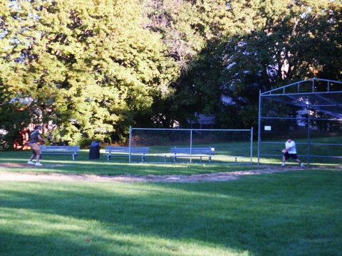 2001 Mercury Grand Marquis - Two people play baseball on a field with benches and trees in the background.