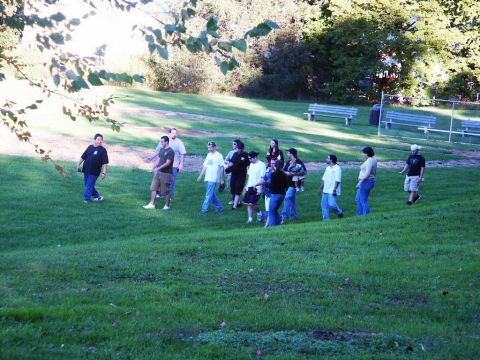 2001 Mercury Grand Marquis - A group of people are seen walking across a grassy area, with trees and park benches in the background.