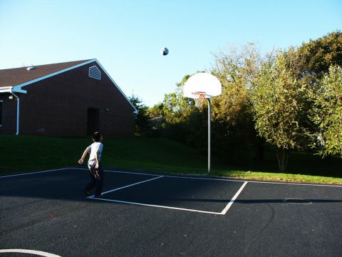 2001 Mercury Grand Marquis - A boy plays basketball on an outdoor court next to a brick building on a sunny day.
