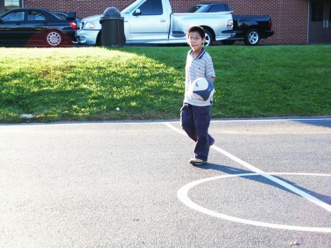 2001 Mercury Grand Marquis - A boy holds a ball on a basketball court with vehicles parked in the background.