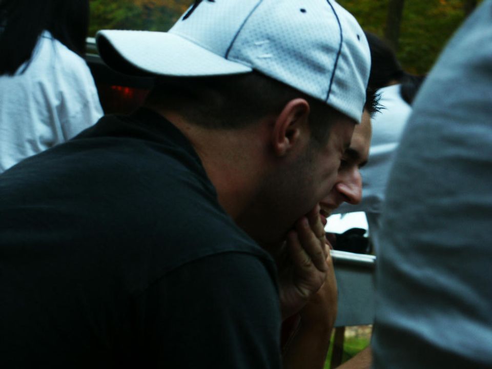 People in casual clothing at an outdoor event, with a partial view of a car's rear quarter panel