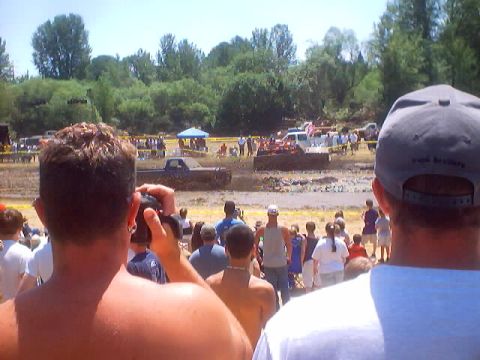 1976 Ford F-100 - A muddy pickup truck navigates a mud pit during an event, with a crowd watching from the sidelines.
